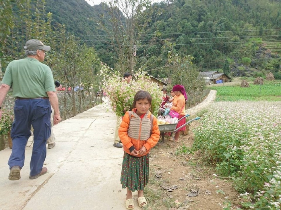 Une scène de village avec des enfants et des adultes marchant sur un sentier entouré de verdure.