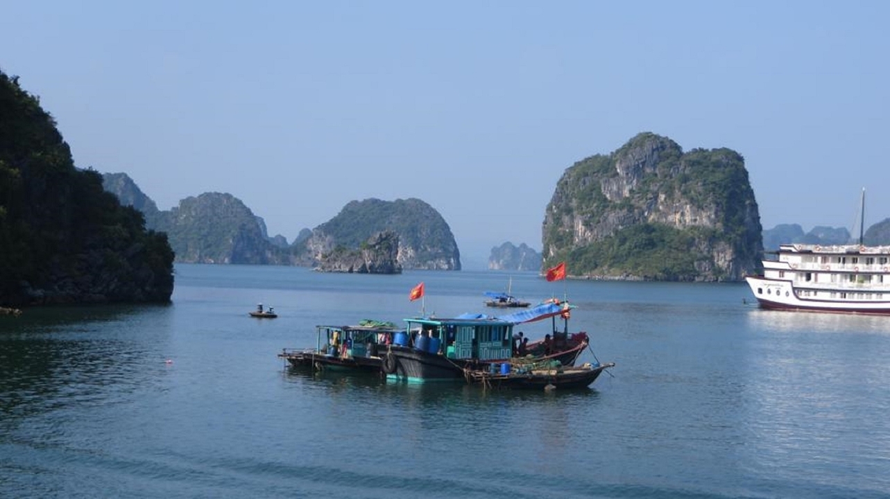 Bateaux sur une baie avec des karsts calcaires en arrière-plan sous un ciel bleu dégagé.