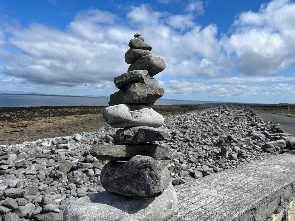 Stacked rock cairn near a road with cloudy sky.