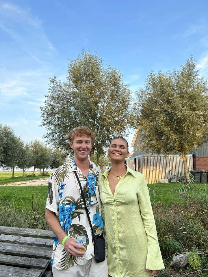 Couple posing in a green park with trees and buildings behind.
