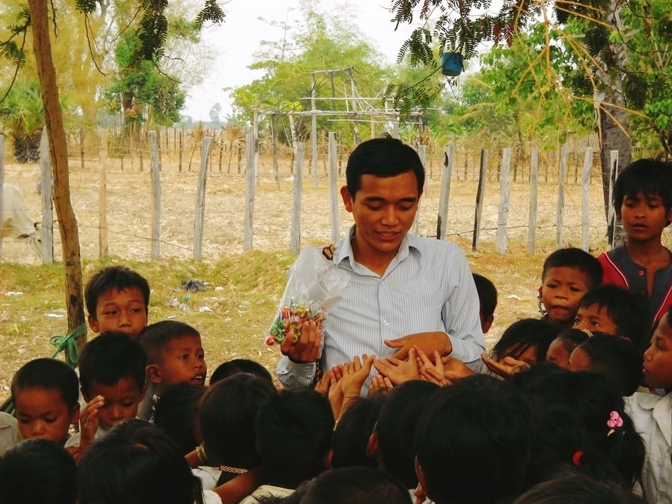 Man distributing items to children outdoors.