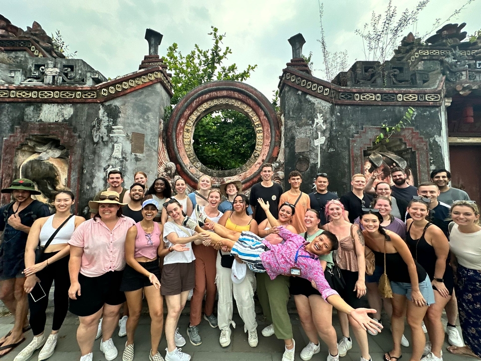Large group of people posing in front of an ancient Vietnamese structure.