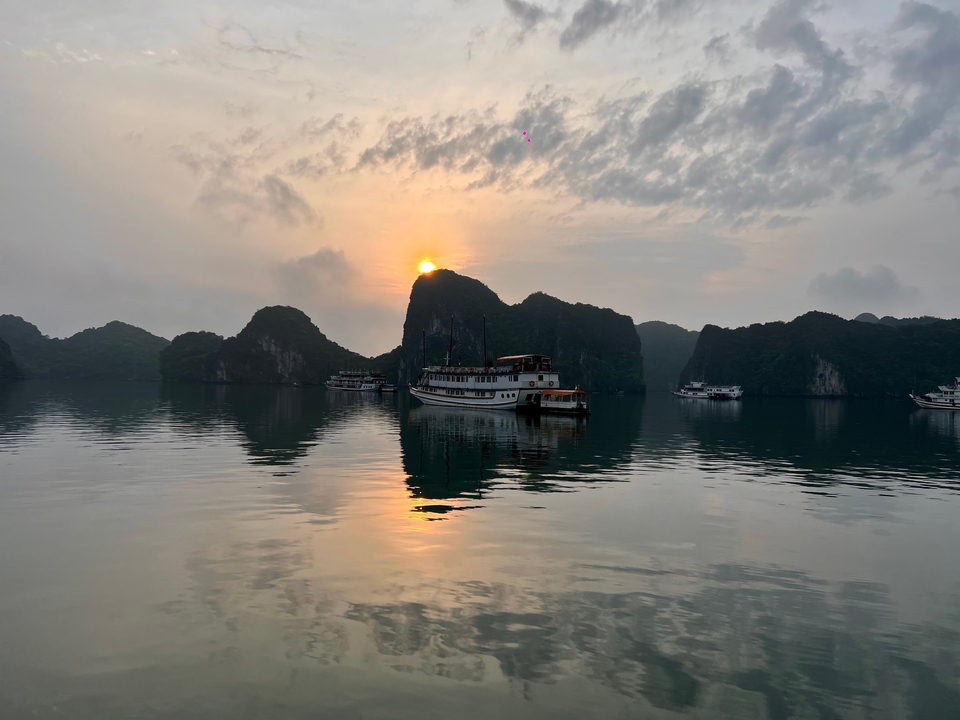 Boats on a calm bay with the sun setting behind limestone karsts.
