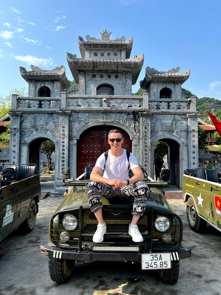 Person sitting on a military vehicle with Vietnamese temple in the background.
