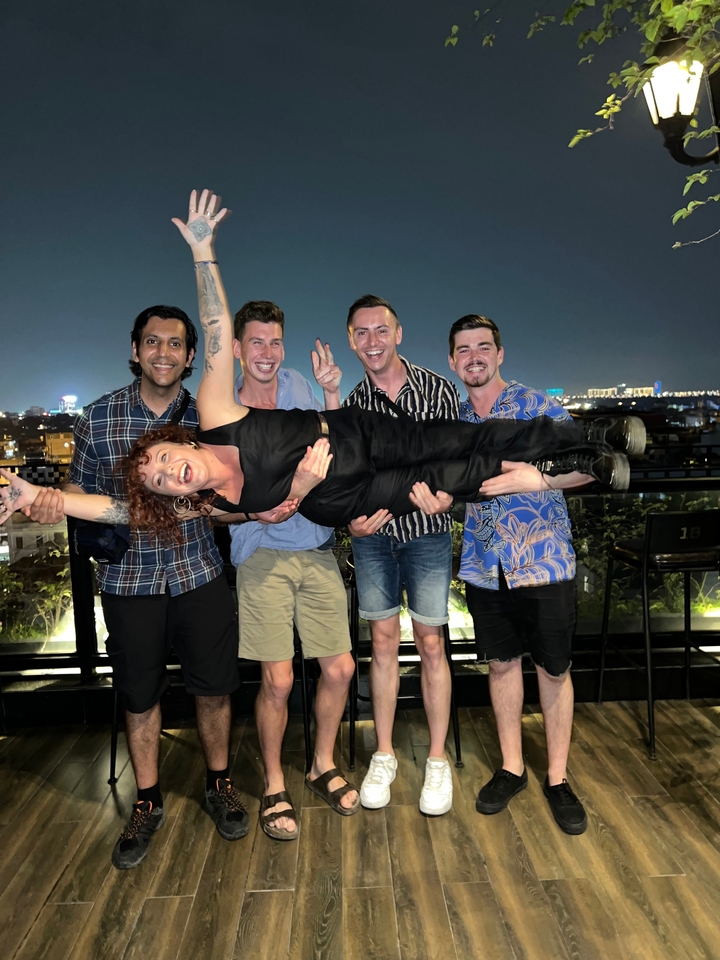 A group of friends lifting someone with a nighttime cityscape.