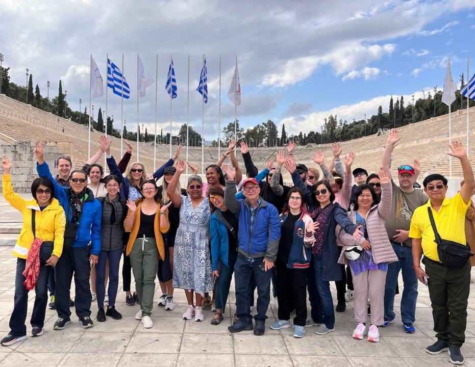 Group of people posing with Greek flags in the background.