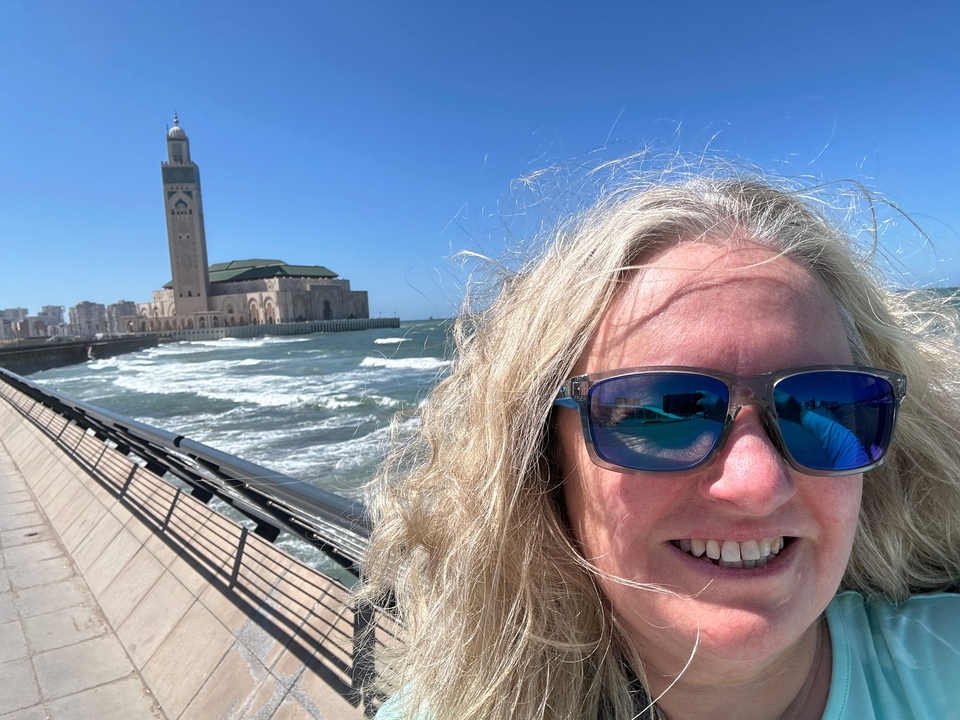 Person taking a selfie near a waterfront with a large mosque in the background.