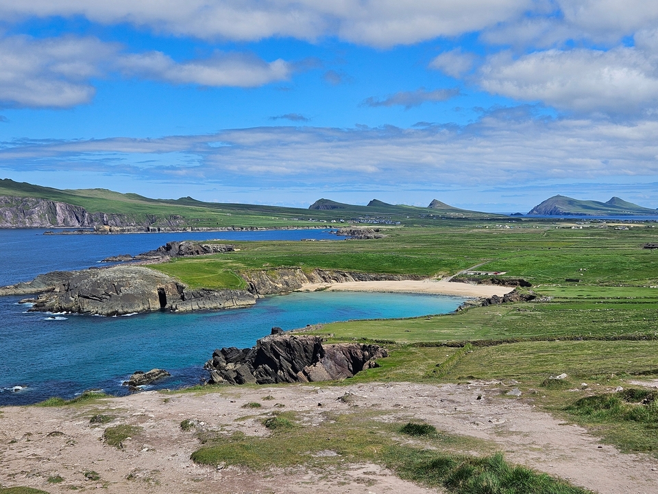 Coastal landscape with beach, cliffs, and grassy hills.