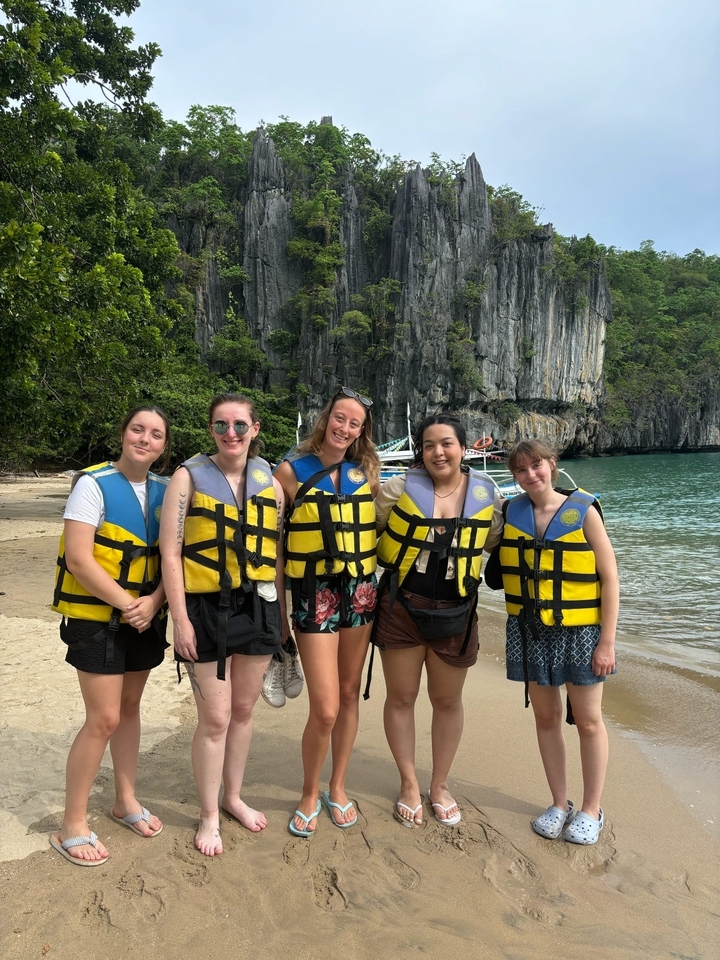 Groupe de cinq personnes en gilets de sauvetage sur une plage avec des falaises.