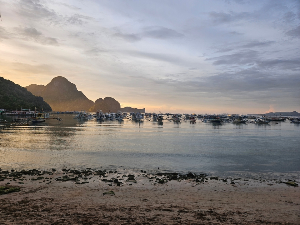 Coucher de soleil sur un port avec des bateaux et des falaises au loin.
