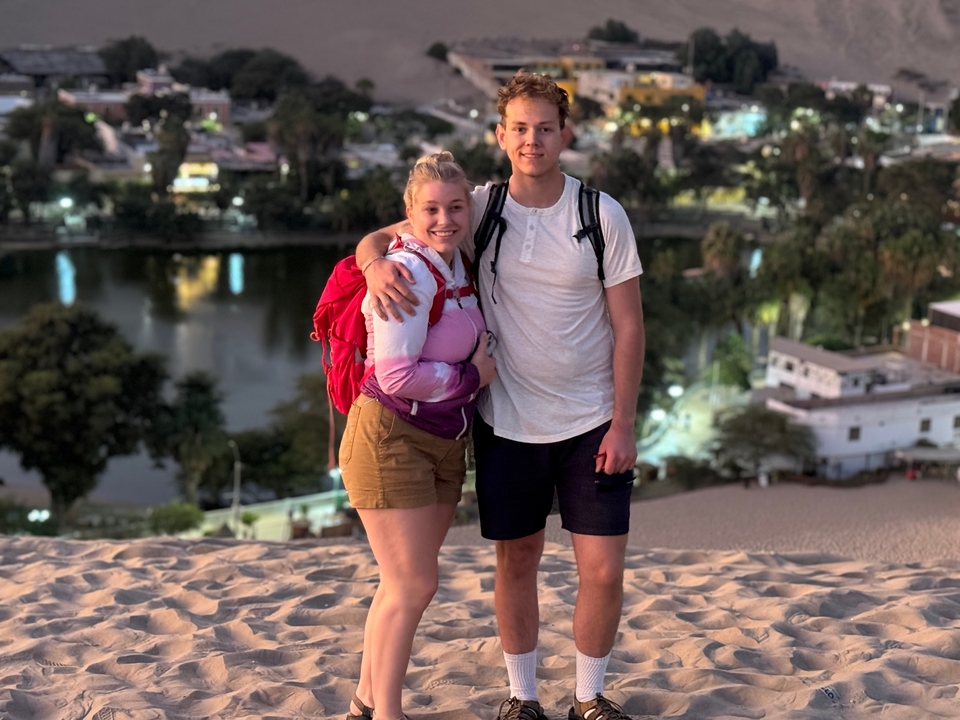 Couple posing on a sand dune with an oasis in the background.