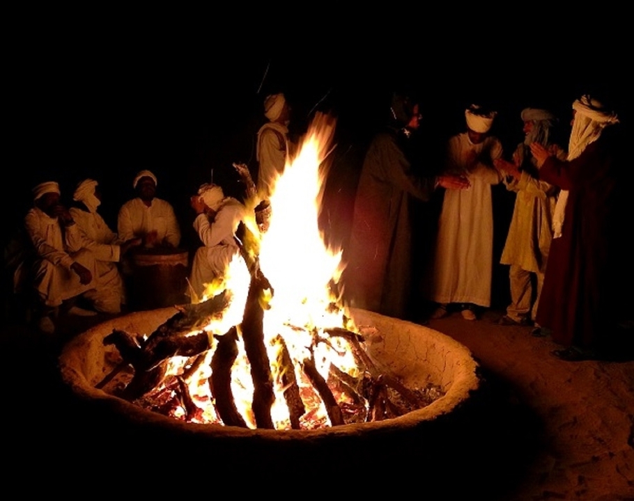 Groupe de personnes en vêtements traditionnels autour d'un feu de camp la nuit.