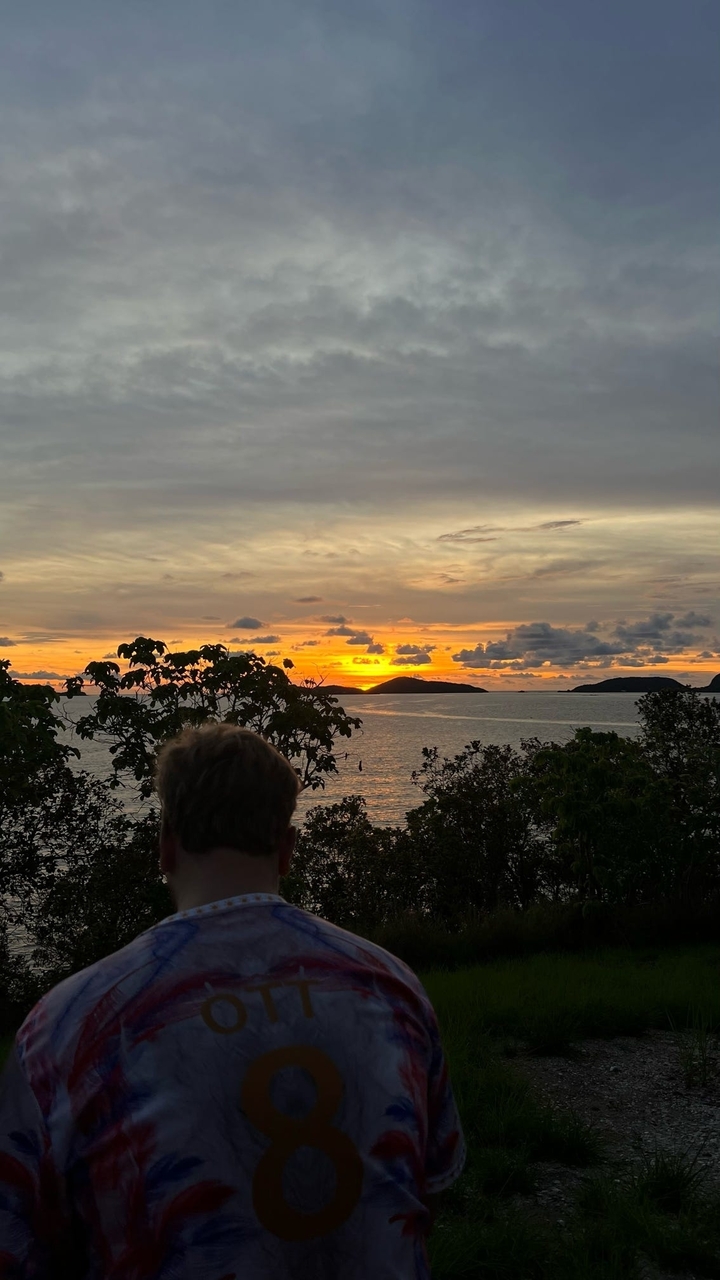 Personne observant un coucher de soleil sur l'océan avec des îles en silhouette à l'arrière-plan.