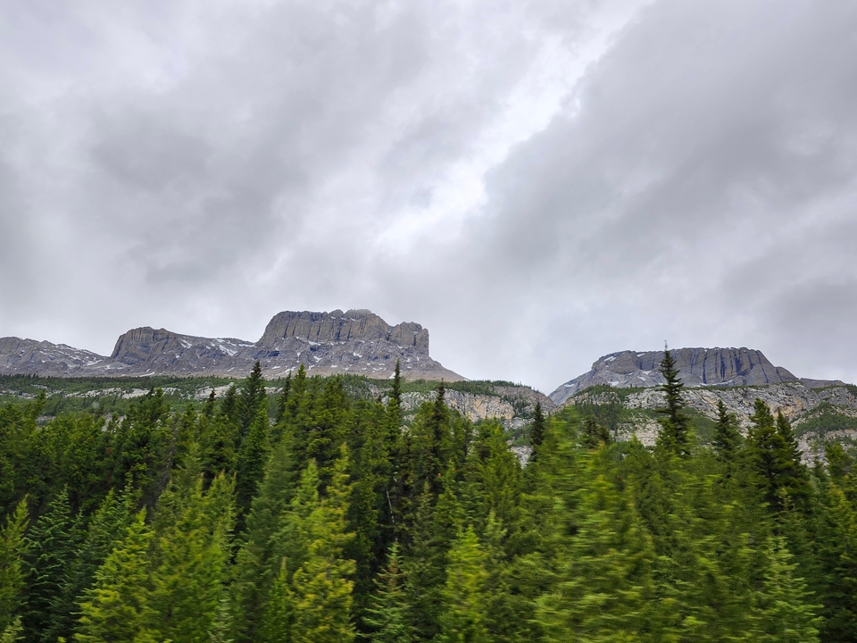 Mountain range with forested foothills under a cloudy sky.