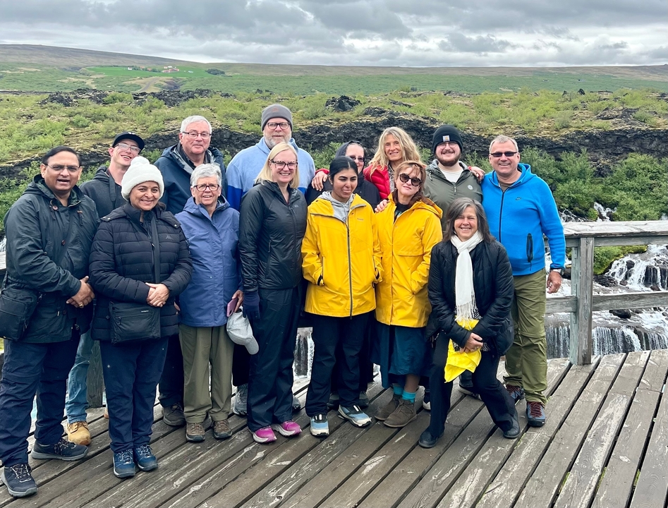 Group of tourists in front of a waterfall wearing jackets.