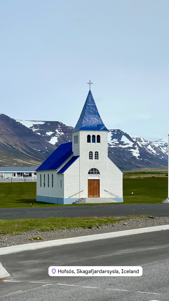 Small church with a blue roof set against mountains.