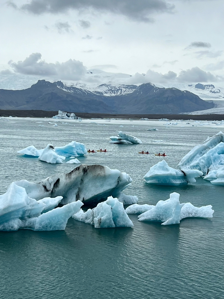 Kayakers navigating icy waters among icebergs.