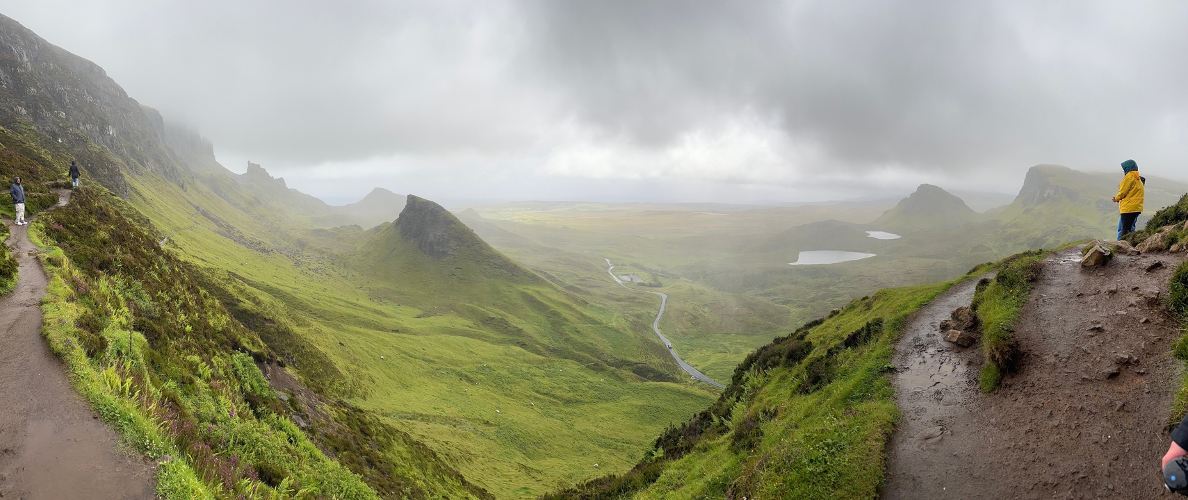 Vast green valley with winding road under a cloudy sky.
