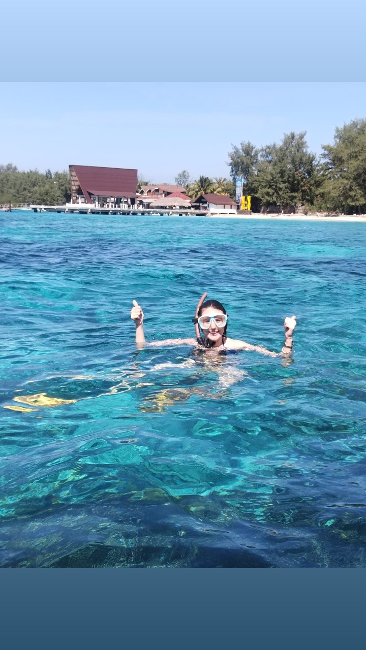 Person giving a thumbs up while snorkeling in clear blue water.