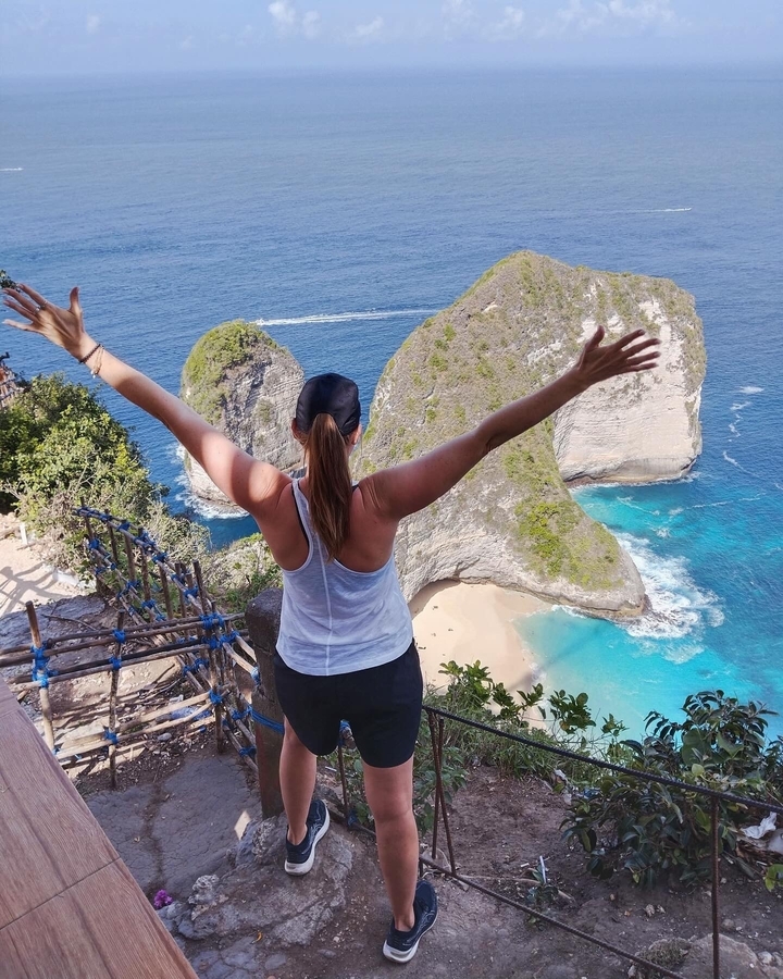 A person raising arms overlooking a scenic coastal view.
