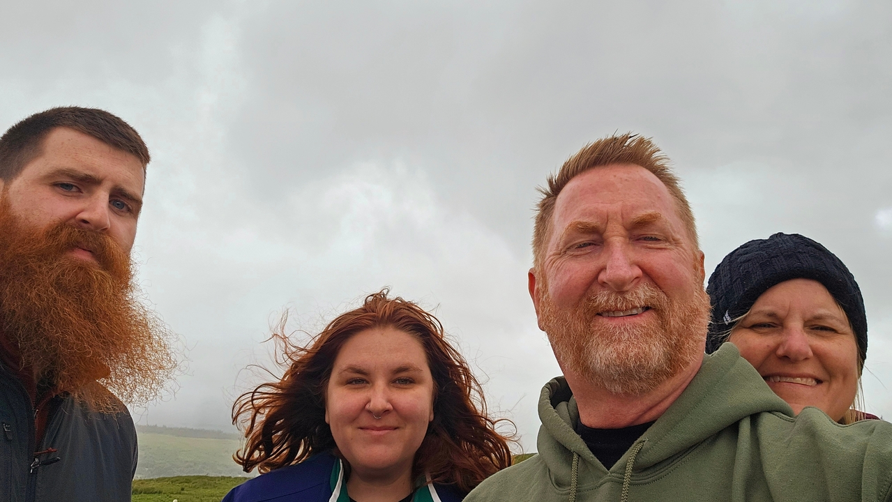 Four people posing together with a cloudy sky backdrop.