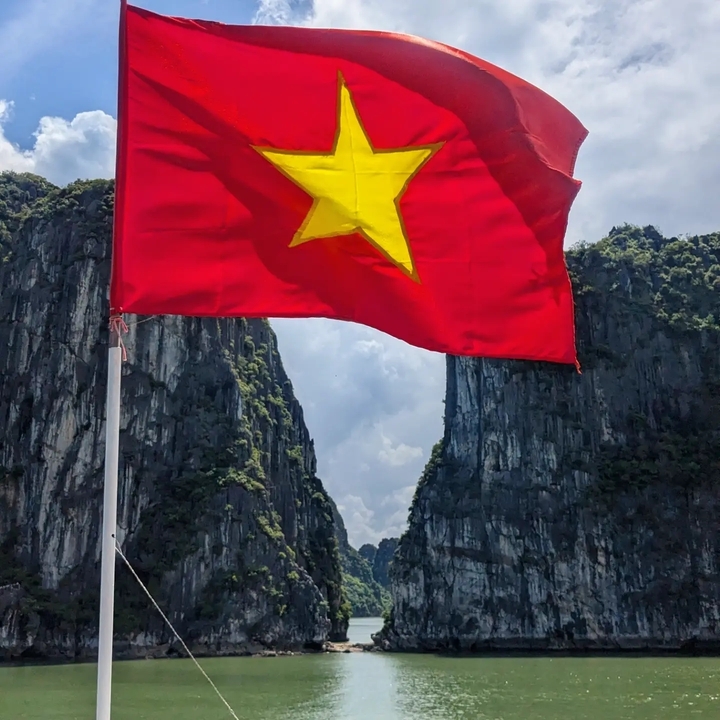 Vietnamese flag flying in front of towering limestone cliffs.