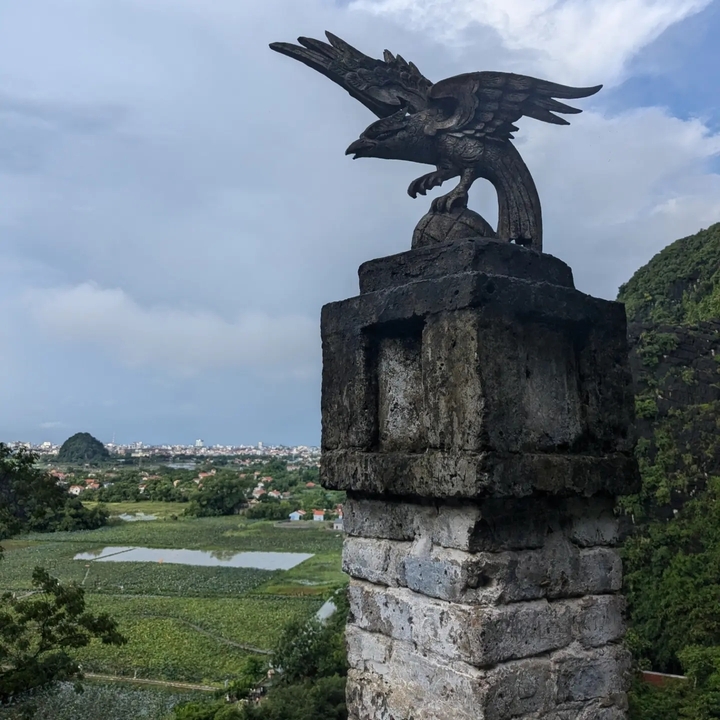 A stone sculpture overlooking a valley with a city in the distance.