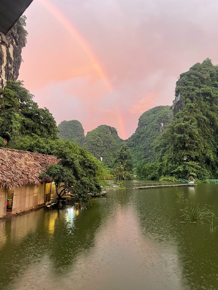 A serene landscape with a lake, lush greenery, and a rainbow at sunset.