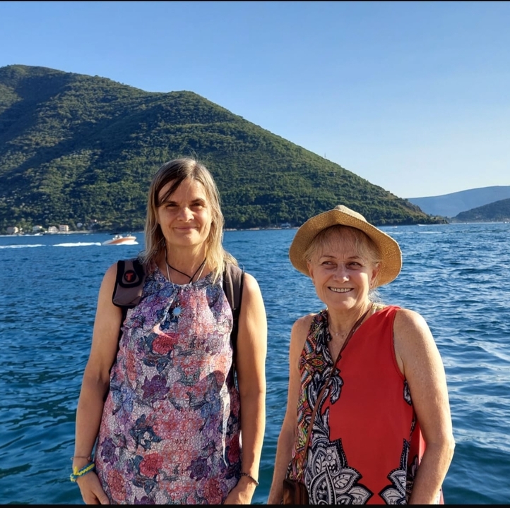 Deux femmes souriantes avec une montagne et la mer en arrière-plan.