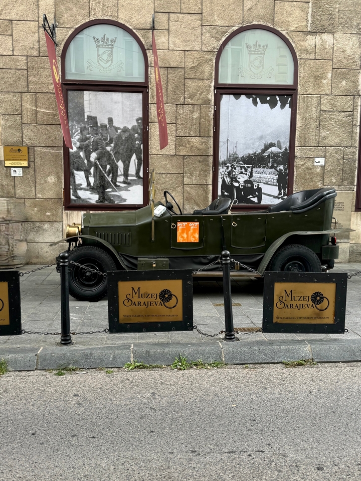 Voiture historique devant un musée avec des photos de guerre.