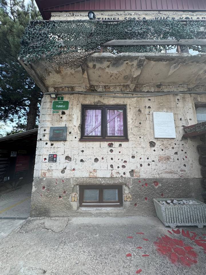 Façade de bâtiment avec des impacts de balles et des rideaux roses aux fenêtres.