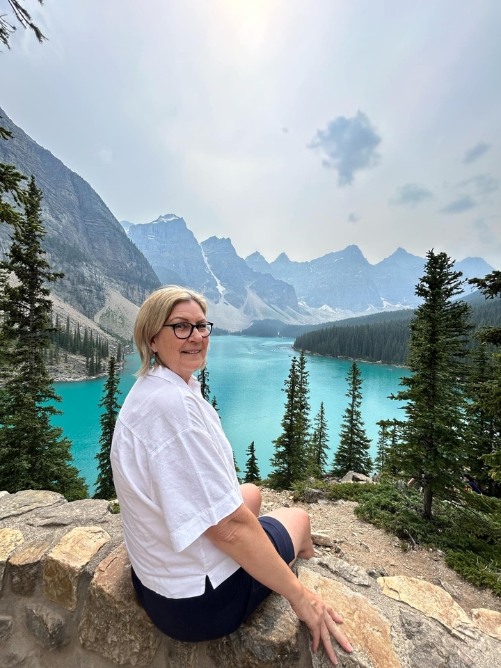 Woman posing with a scenic view of a lake and mountains.
