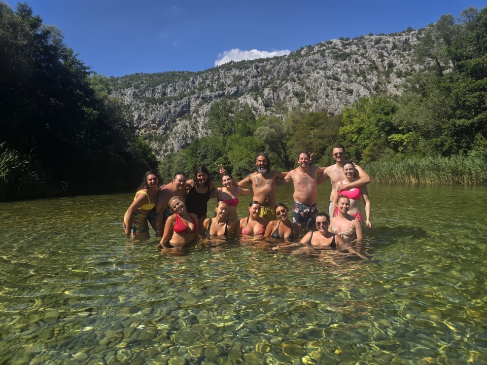 Group of people in a river surrounded by greenery and cliffs.