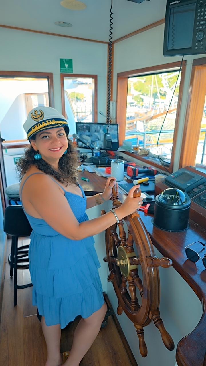 Woman in a captain's hat at a ship's helm.