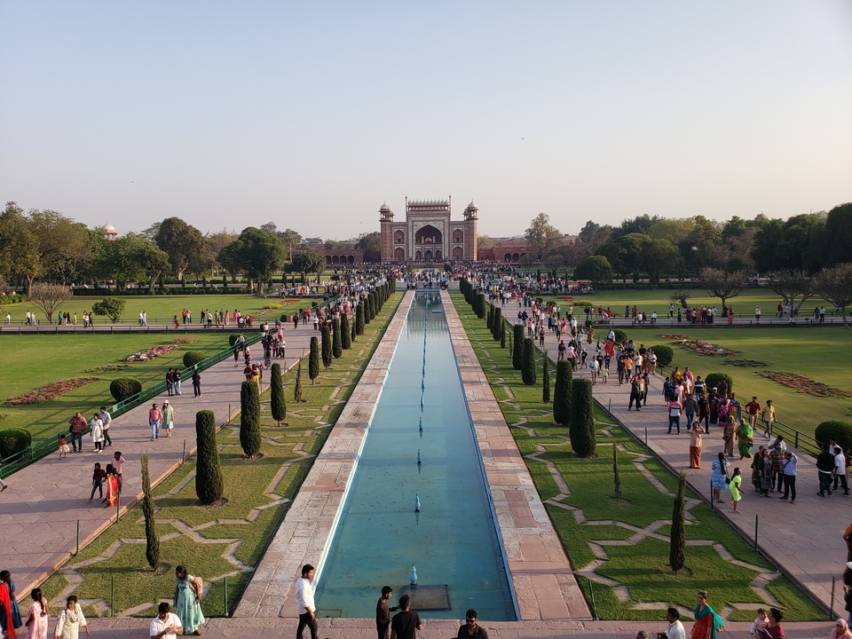 Un jardin avec un bassin de réflexion et une porte d'entrée en arrière-plan, bondé de visiteurs.