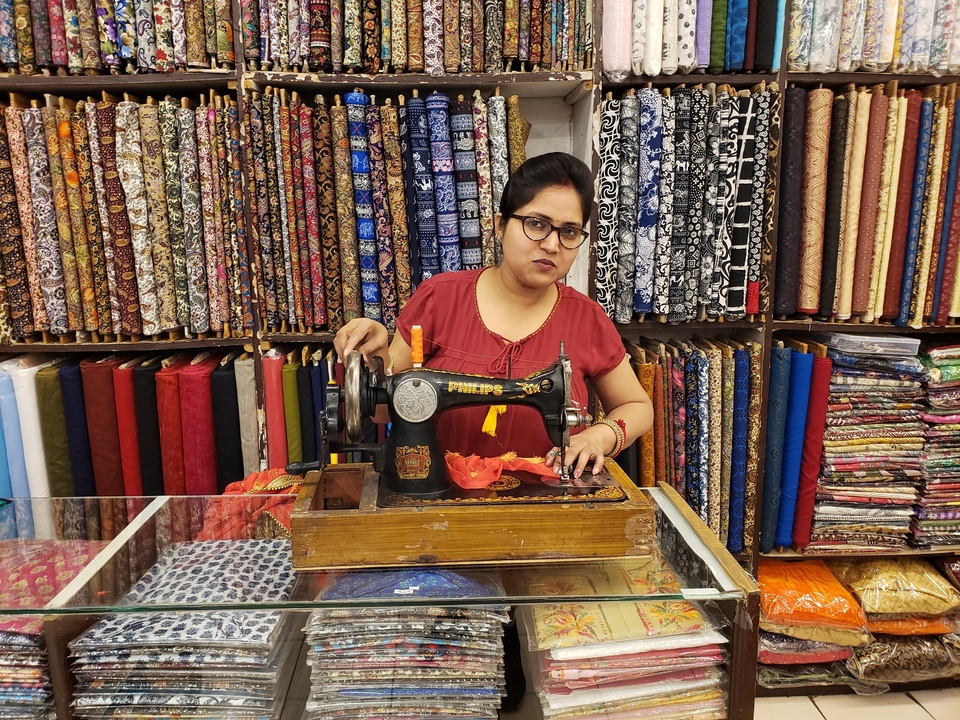 Une femme utilisant une vieille machine à coudre avec des tissus colorés suspendus derrière.