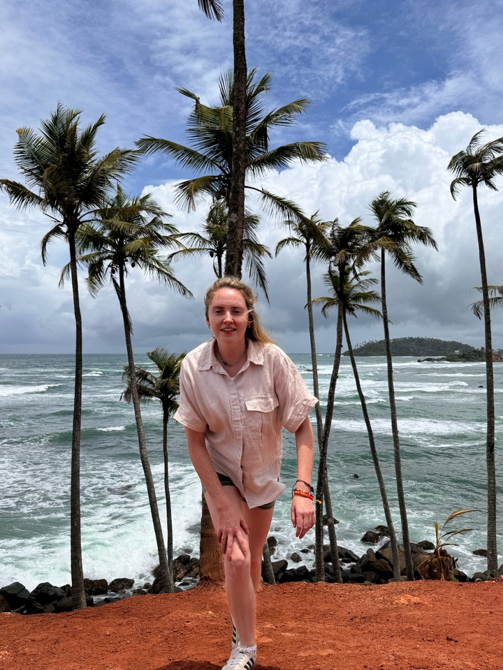 Woman standing on a beach with palm trees and ocean waves.
