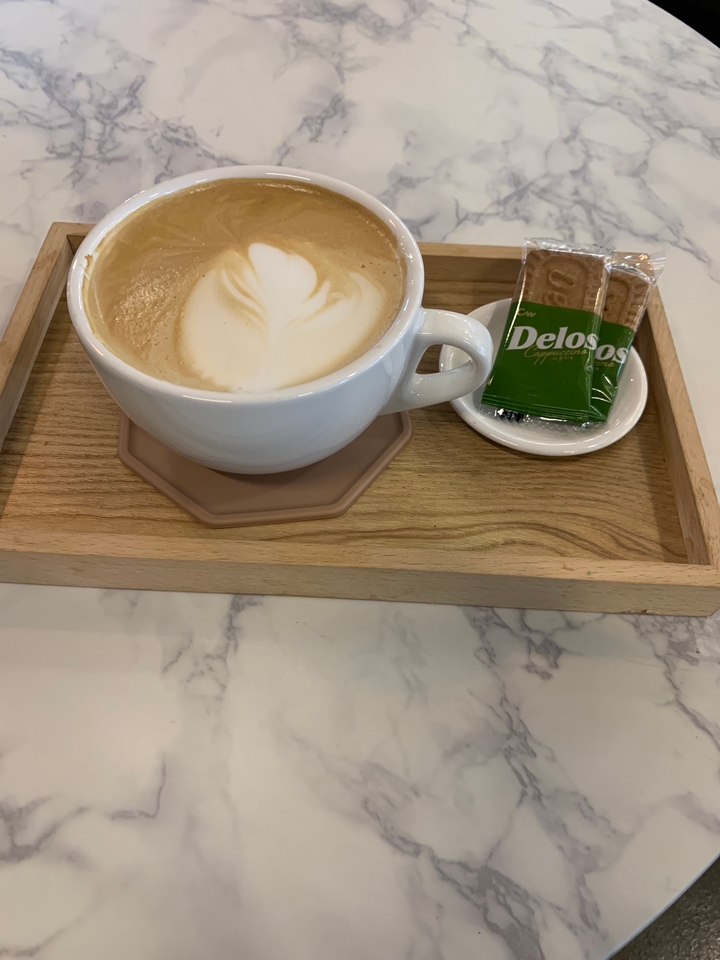 Gros plan d'un cappuccino avec un biscuit sur un plateau en bois.