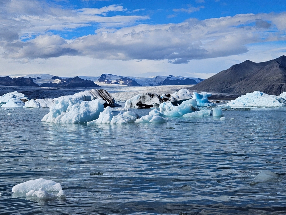 Icebergs floating in a glacial lagoon with mountains in the distance.