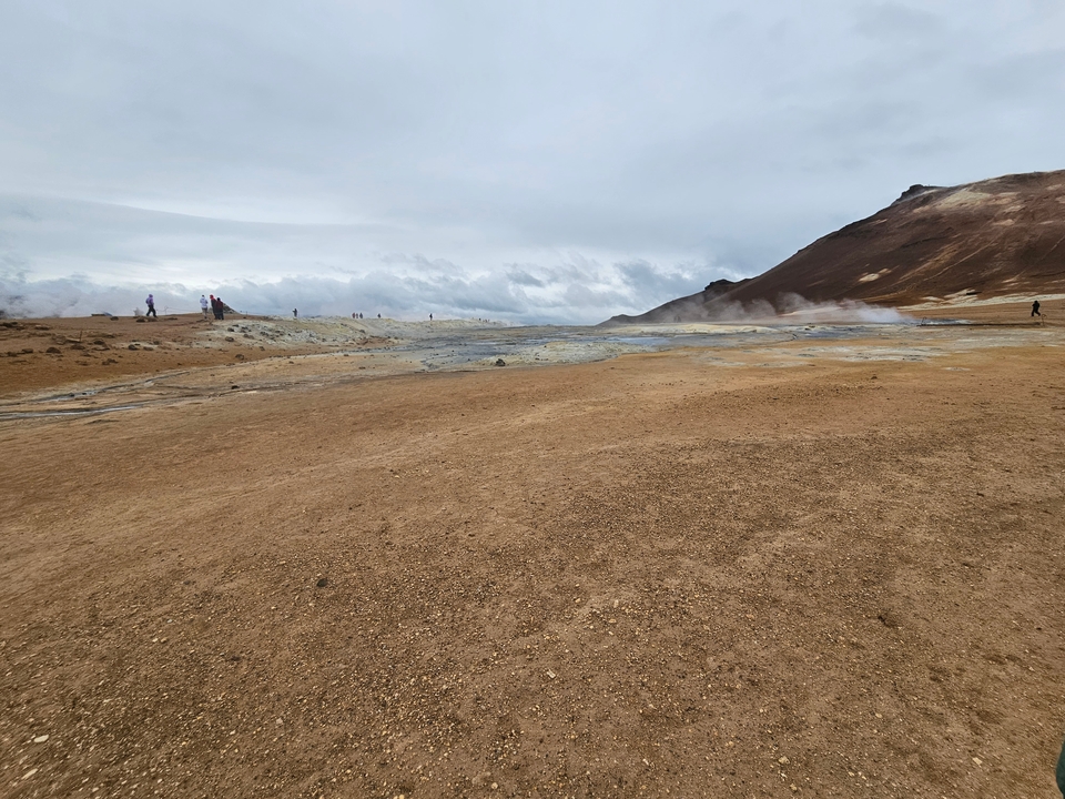 Geothermal area with steaming ground and distant hills.