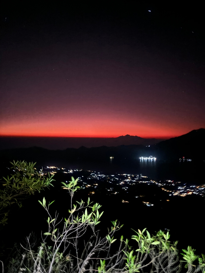 Night view of a town with a red sky and distant mountains.