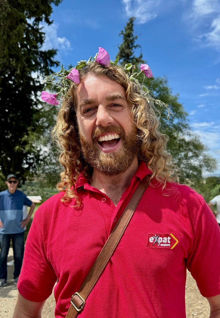 Une personne portant une chemise rouge avec une fleur dans les cheveux souriante à l'extérieur.