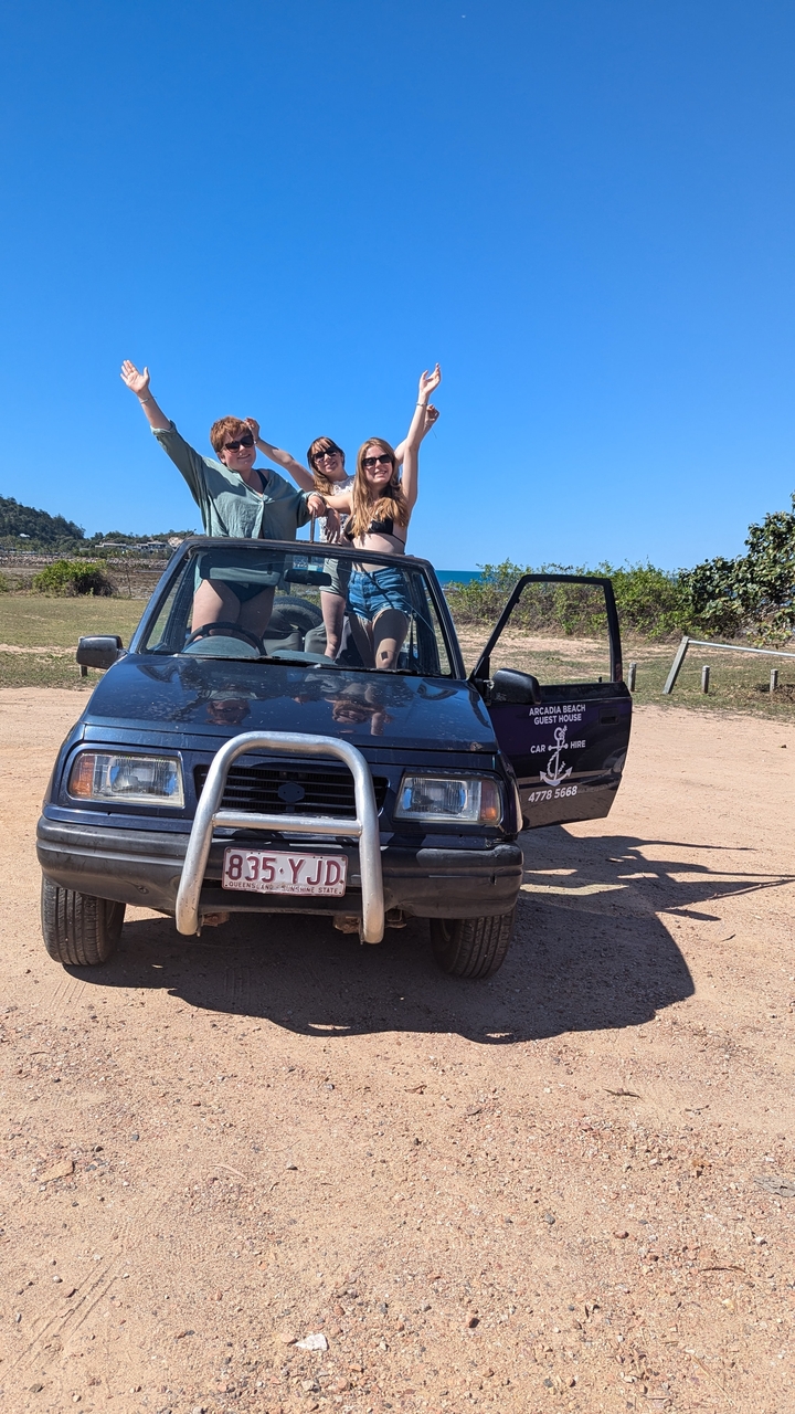 Two people standing next to a jeep with a beach background.