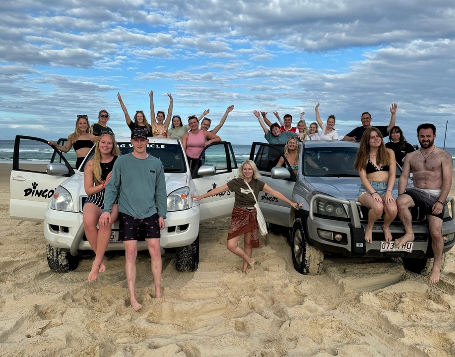 Group of people posing with 4WD vehicles on a sandy area.