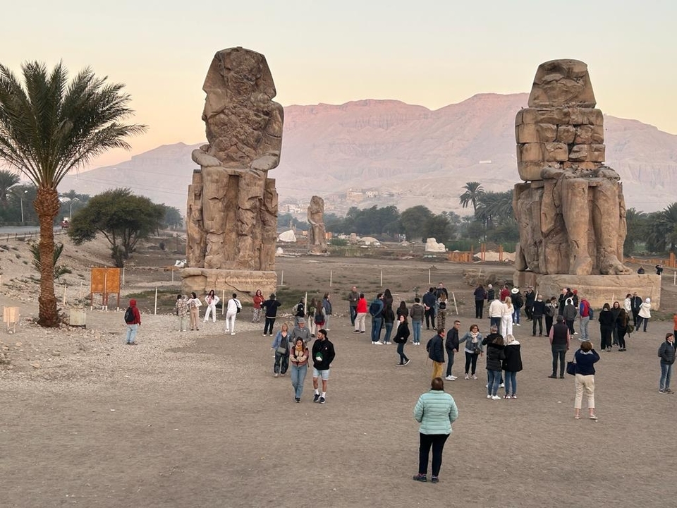 Des gens marchent près de deux grandes statues de pierre dans un paysage aride.
