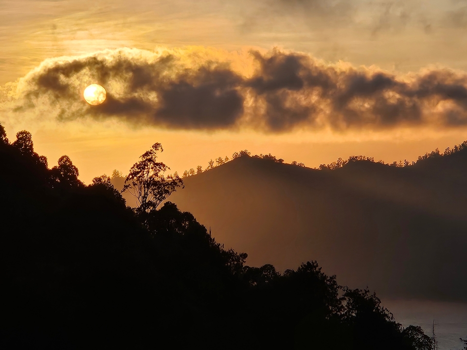 Dramatic sunset over hills with the sun peeking through clouds