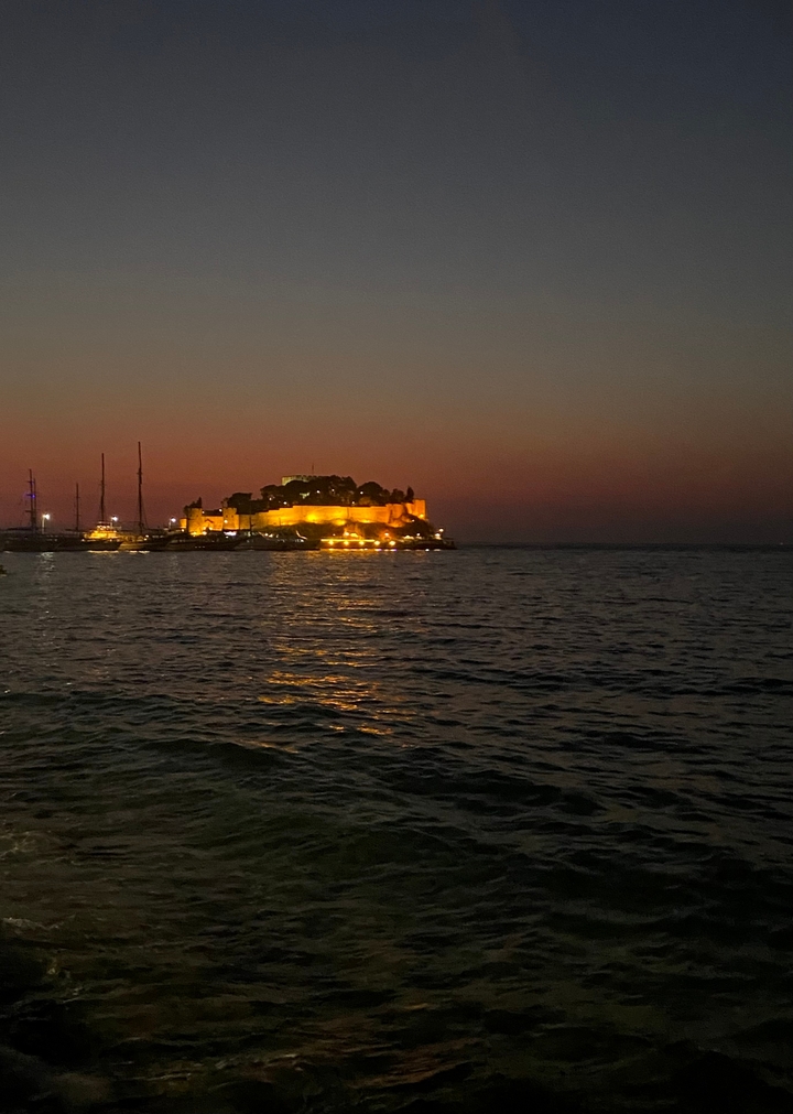 Forteresse illuminée sur une île au coucher du soleil, avec de l'eau environnante.