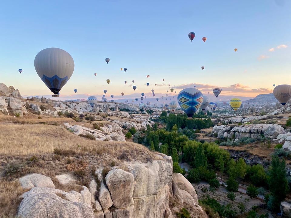 Nombreux ballons à air chaud survolant un paysage pittoresque au lever du soleil.