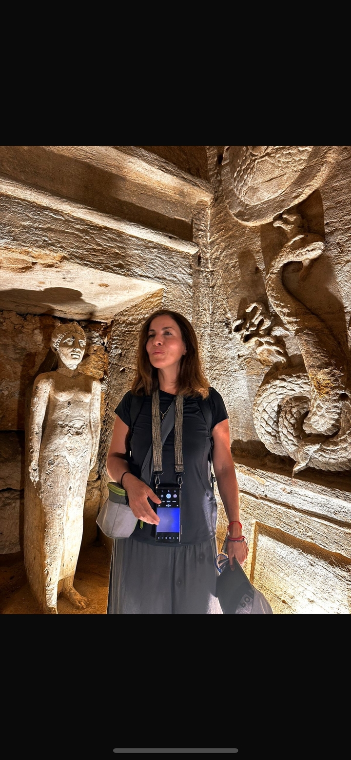 Une femme explorant une grotte avec des statues sculptées et de l'art mural.