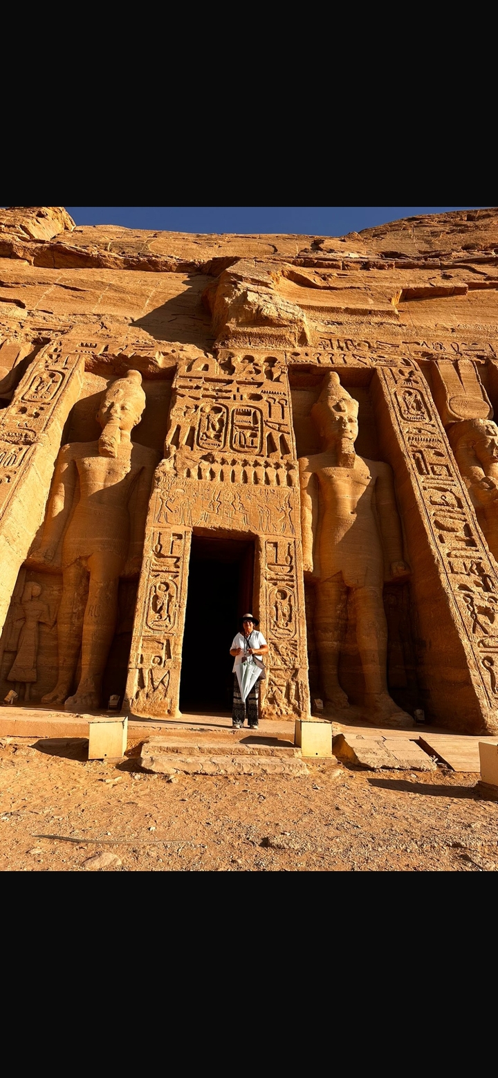 Un homme debout devant le temple d'Abou Simbel avec de grandes statues.
